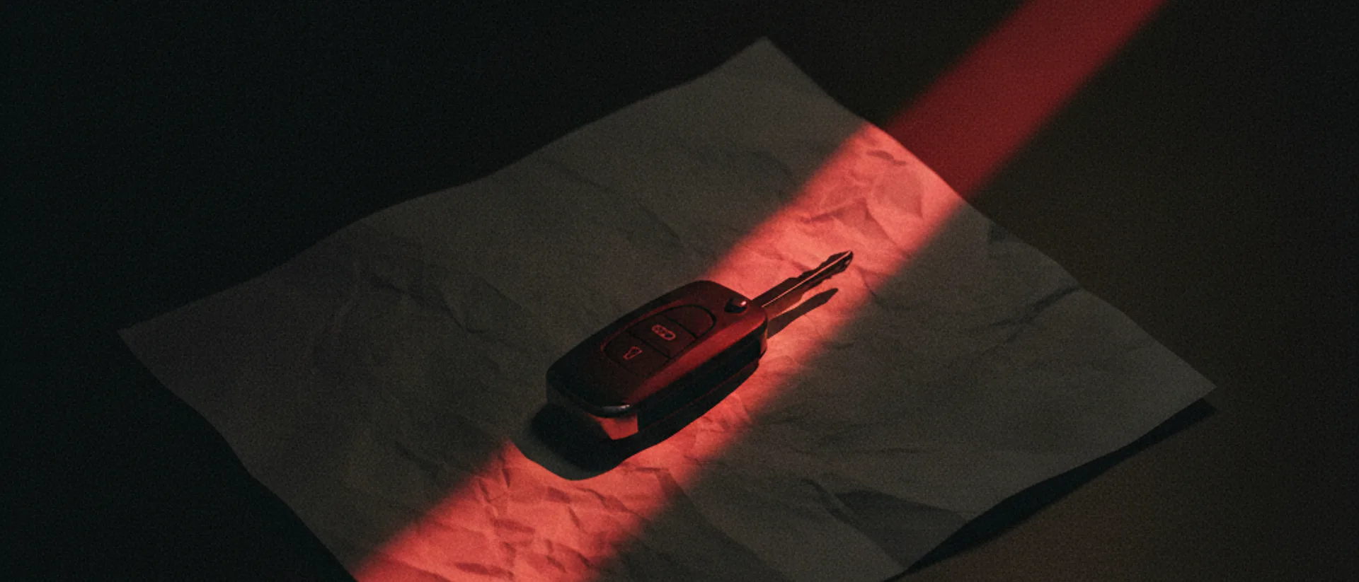 Chave de veículo sobre documento em mesa escura, iluminada por uma luz vermelha rasante