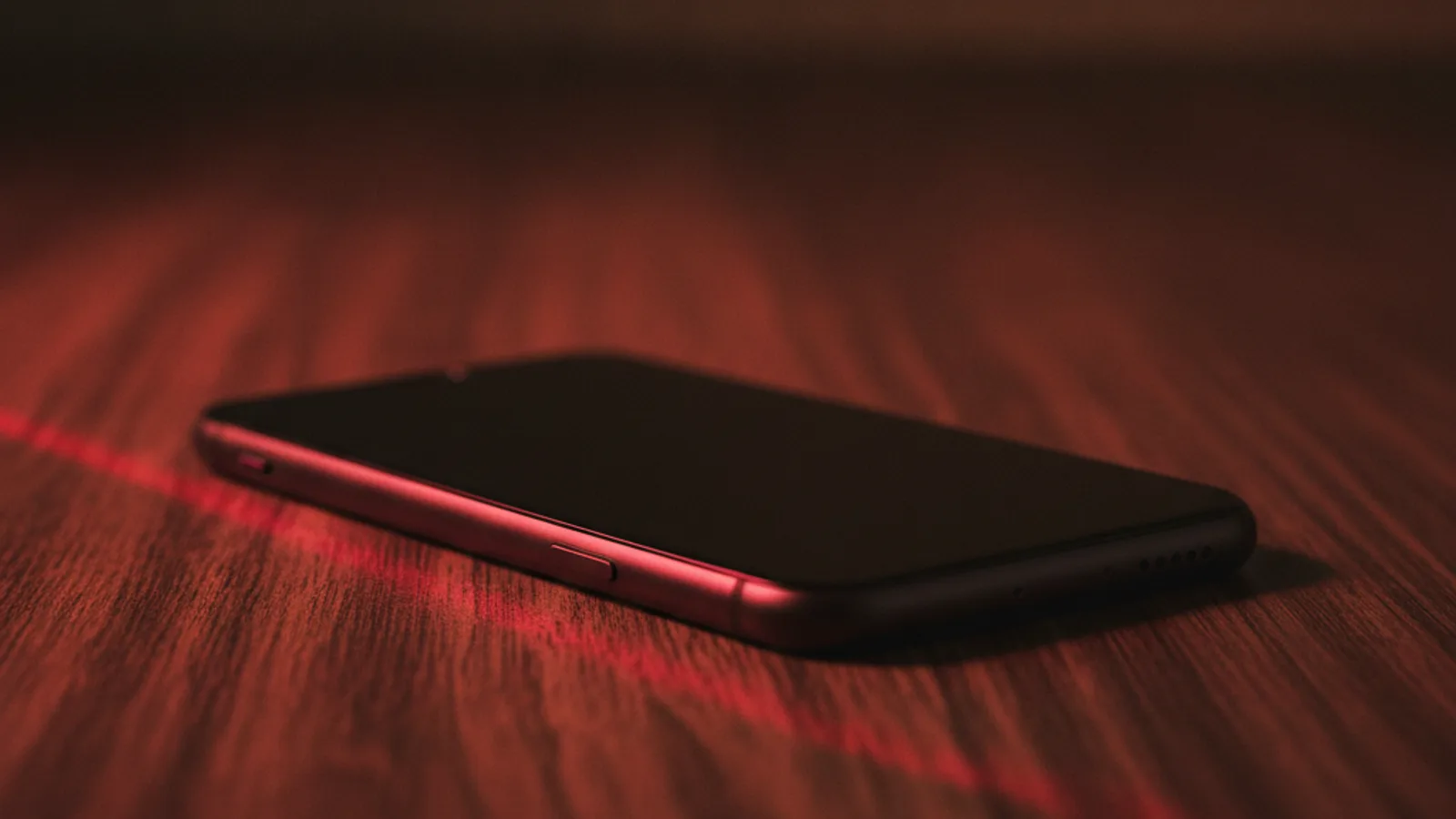 Celular escuro virado para baixo sobre mesa, com feixe de luz vermelha