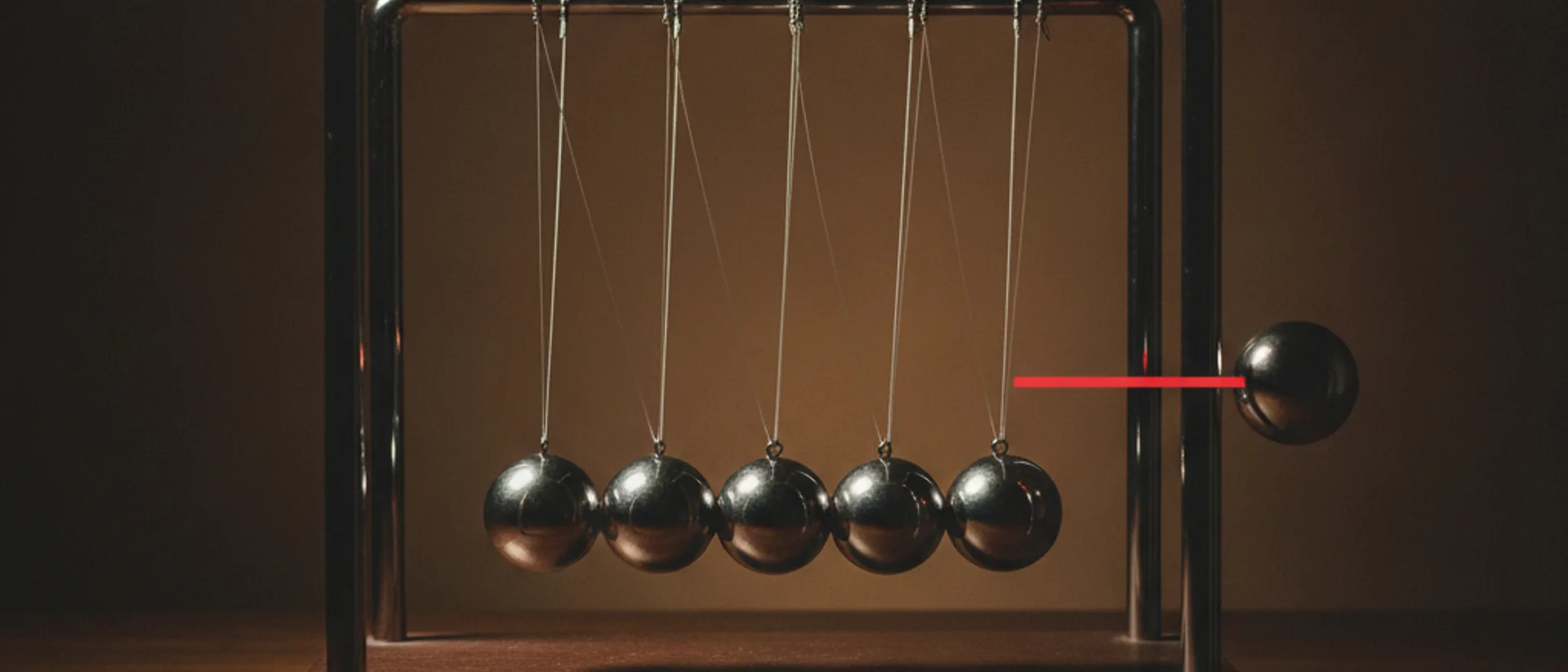 Berço de Newton com cinco esferas de aço encostadas e uma sexta afastada e imóvel, separada das demais por uma faixa de luz vermelha